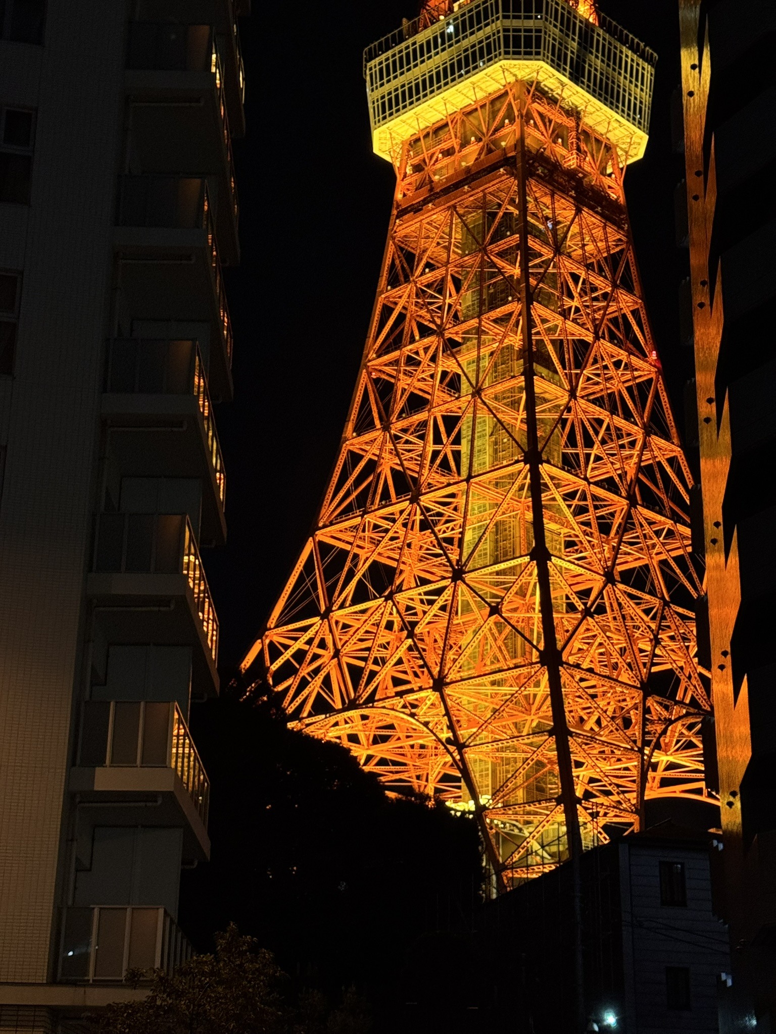 Tokyo Tower illuminated at night between nearby buildings.